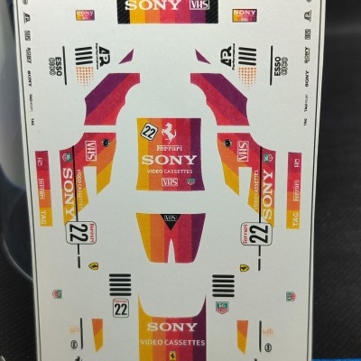 Folha de autocolantes para modelo de carro de corrida Ferrari com logótipos Sony, Ferrari, VHS e outros.