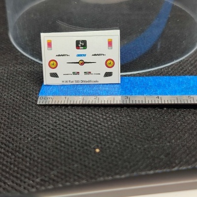Folha de autocolantes para miniaturas com logótipos Fiat e Abarth, sobre superfície preta texturada com régua e fita azul