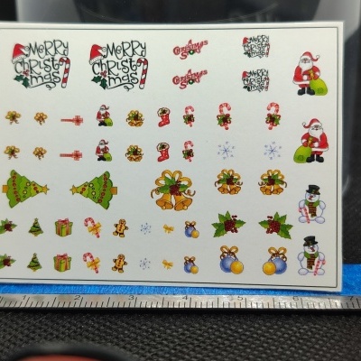 Folha com autocolantes pequenos de Natal coloridos e mensagens em inglês, com régua para medir ao fundo.