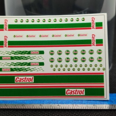 Folha de autocolantes Castrol em verde, vermelho e branco com régua azul em fundo escuro.