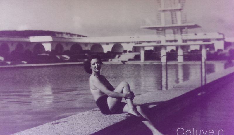 Mulher sentada no cais com barcos e ponte ao fundo em foto preto e branco
