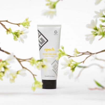 Frasco branco de produto Epoch com tampa preta entre ramos floridos