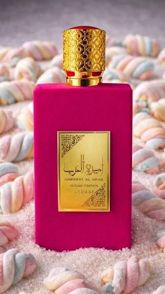Asdaaf Ameerat Al Arab Sugar Crown Eau De Parfum 100ml For Women Frasco de perfume rosa com tampa dourada e rótulo dourado, rodeado de marshmallows coloridos