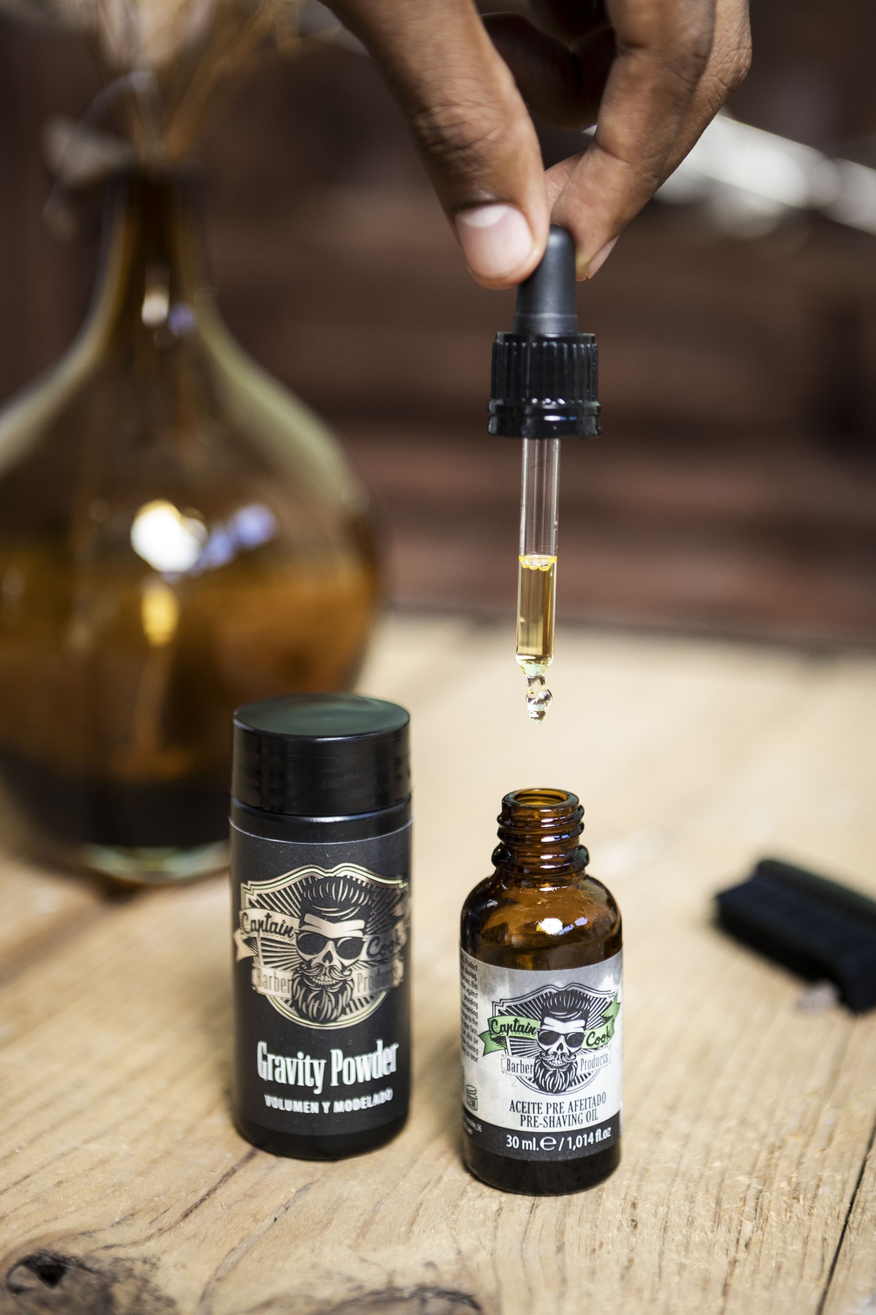 Óleo pré barbear 30 ML CAPTAIN COOK Frasco de óleo pré-barba com conta-gotas e recipiente de pó Gravity Powder sobre mesa de madeira.