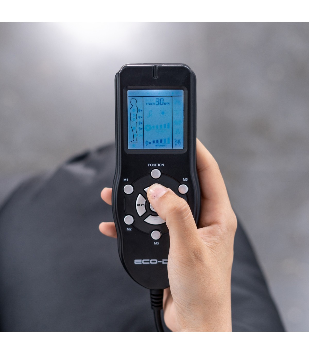 Poltrona de Massagem Relax Monaco – 10 Vibromotores, Reclinável 160°, Calor Lombar, Programas Automáticos, Controle Remoto Comando remoto preto com ecrã digital azul e botões circulares segurado por mão