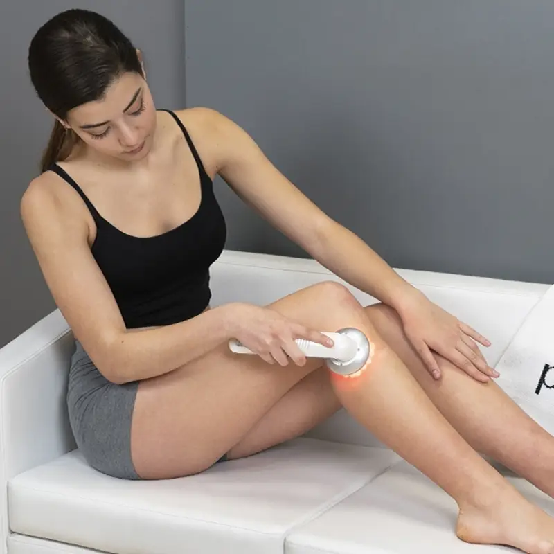 ItalianDesign aparelho Ultrassons, Fototerapia e Galvânica Mulher a usar dispositivo LED branco para massagem na perna sentada em sofá branco