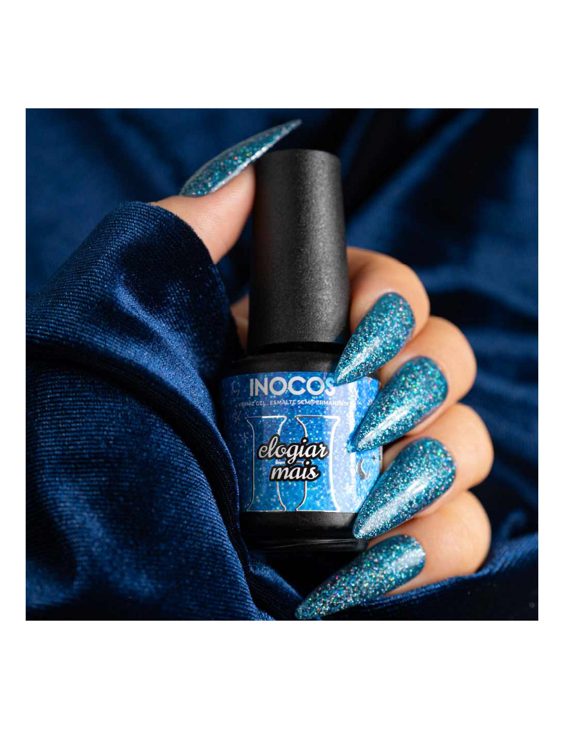 Verniz Gel Inocos A Million Dreams 15ml Elogiar Mais MD4 Frasco de verniz INOCOS azul glitter segurado por mão com unhas compridas azuis glitter em fundo azul