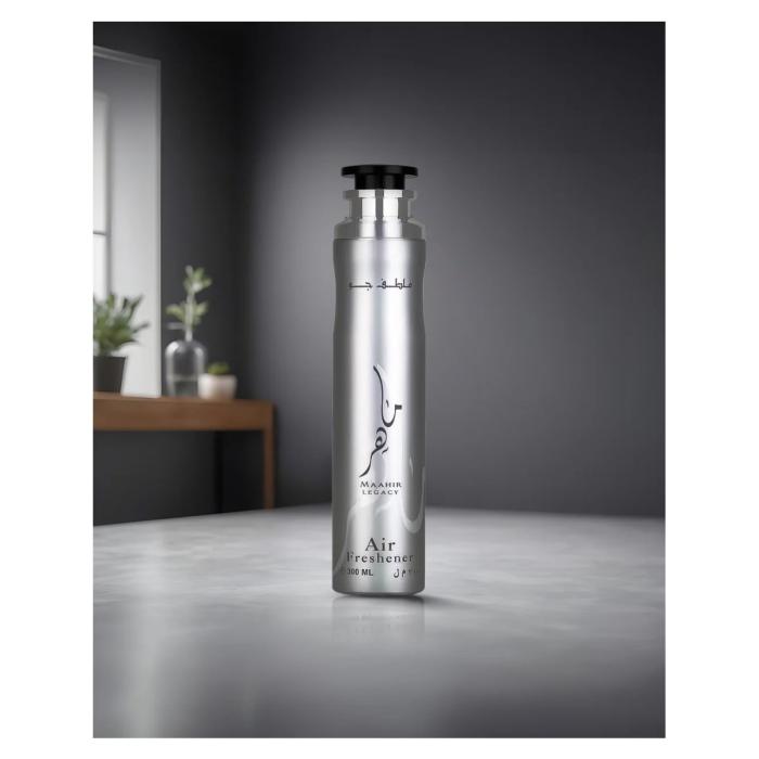 Lattafa Maahir Legacy Air Freshener 300 ml Frasco prateado de ambientador sobre superfície cinza com fundo cinza e plantas desfocadas.