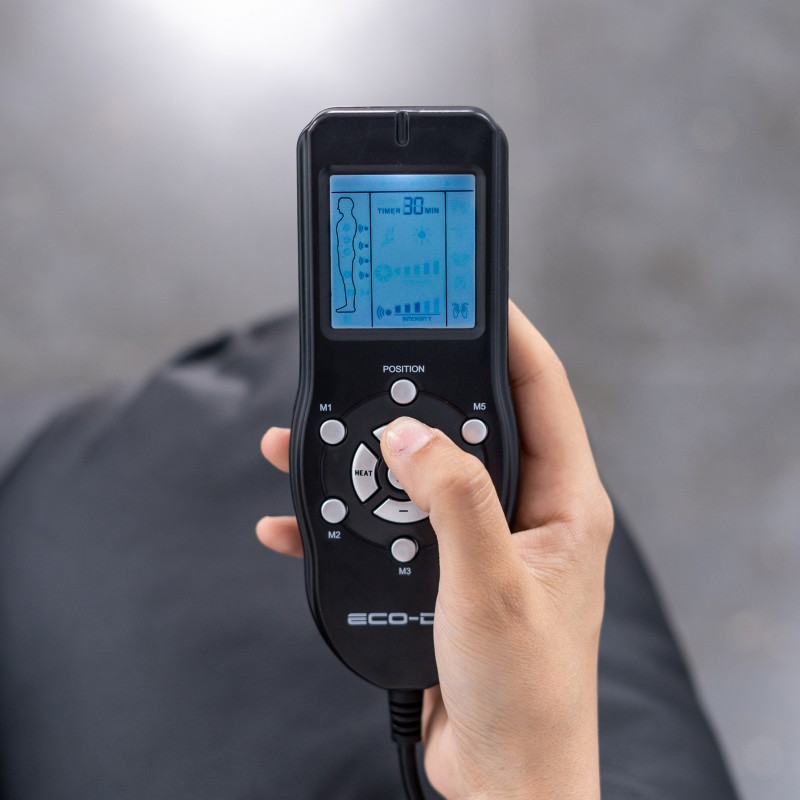 Poltrona de Massagem 8590 UP Comando remoto preto com ecrã digital azul mostrando figura humana e texto, segurado por mão