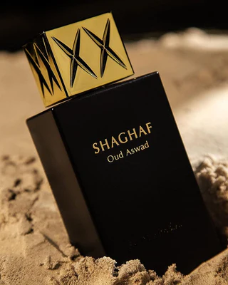 Shaghaf Oud Aswad - Swiss Arabian Unisex Frasco preto de perfume SHAGHAF Oud Aswad com tampa dourada decorada, sobre areia