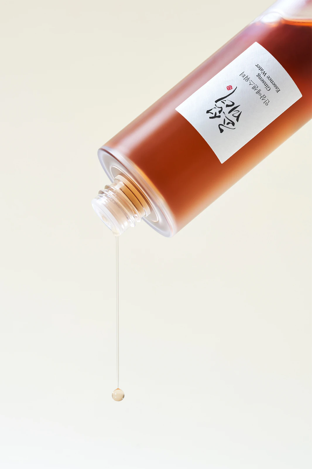 Beauty Of Joseon Ginseng Essence Water 150 Ml frasco âmbar derramando líquido, rótulo branco com texto em inglês e caracteres asiáticos
