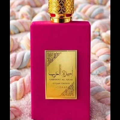 Frasco de perfume rosa com tampa dourada e rótulo dourado, rodeado de marshmallows coloridos