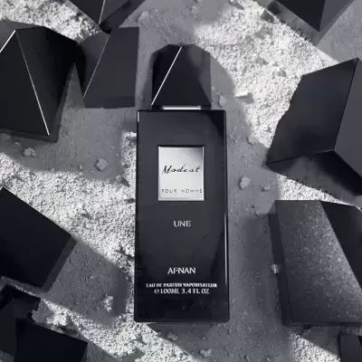 Frasco de perfume preto com texto branco em superfície clara com formas geométricas pretas.