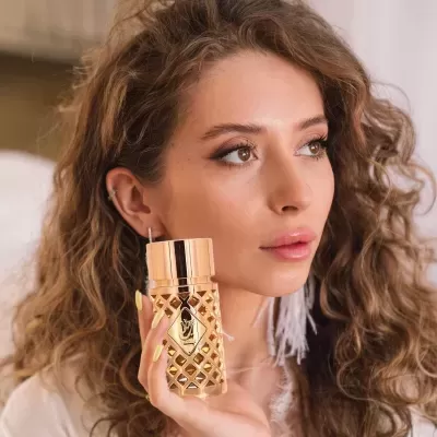 Frasco de perfume dourado segurado por mulher com cabelo encaracolado