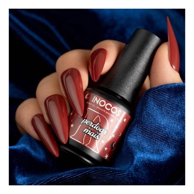 Unhas com verniz vermelho escuro segurando frasco de verniz gel INOCOS em fundo azul