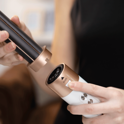 Dispositivo eletrónico de beleza branco e dourado com botão 'PUSH' em mãos