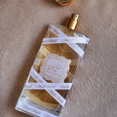 Frasco transparente de perfume com líquido amarelo e tampa dourada removida sobre tecido beige.