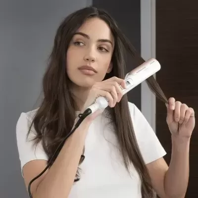 Mulher a usar prancha de cabelo branca e rosa para alisar cabelo comprido