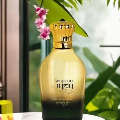 Frasco dourado e preto de perfume WUJOOD sobre base branca com plantas ao fundo
