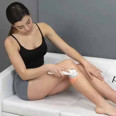 Mulher a usar dispositivo LED branco para massagem na perna sentada em sofá branco
