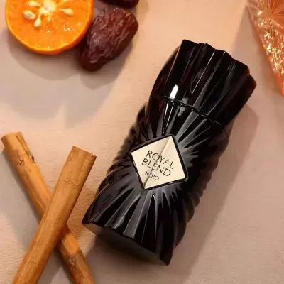 Frasco de perfume preto facetado com etiqueta ROYAL BLEND NERO ao lado de paus de canela e fruta