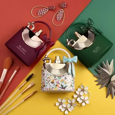 Três frascos de perfume com laços em cima de fundo colorido com pincéis de maquilhagem e brincos.