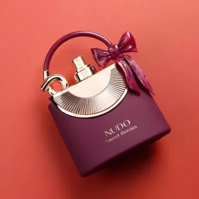 Frasco de perfume roxo com tampa dourada e laço roxo sobre fundo laranja