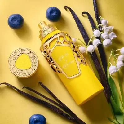 Frasco amarelo de perfume com detalhes dourados e elementos naturais ao redor