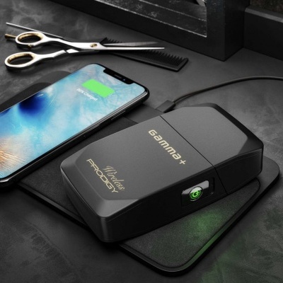 Carregador wireless preto Gamma+ PRODIGY com botão verde num tapete de carregamento, smartphone, tesoura e pente