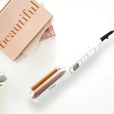 Prancha de cabelo branca e dourada com ecrã digital ao lado de livros rosa
