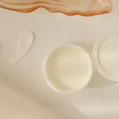 Recipiente de creme branco aberto com espátula pequena e objeto decorativo laranja
