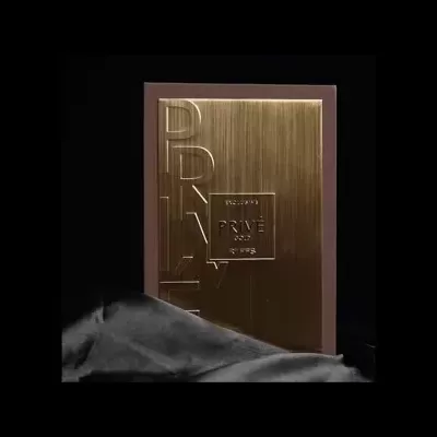 Embalagem metálica dourada com texto PRIVÉ e tecido cinzento ao lado