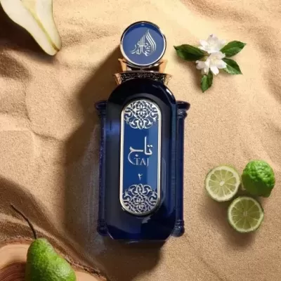 Frasco de perfume azul escuro com detalhes dourados, sobre areia com frutas e flores ao redor
