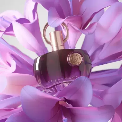 Frasco de perfume roxo escuro com tampa dourada rodeado por pétalas de flor lilás