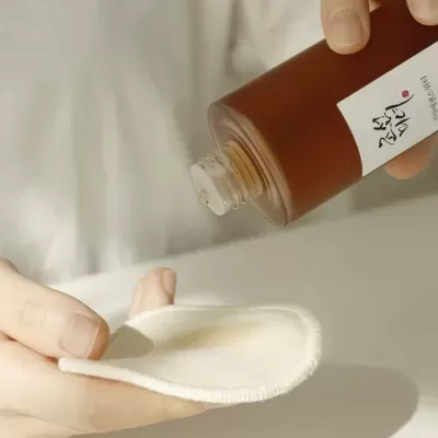 Frasco castanho com líquido a ser despejado em almofada de tecido creme
