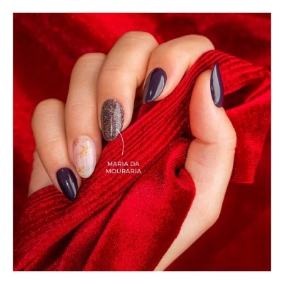 Mão com unhas decoradas segurando tecido de veludo vermelho