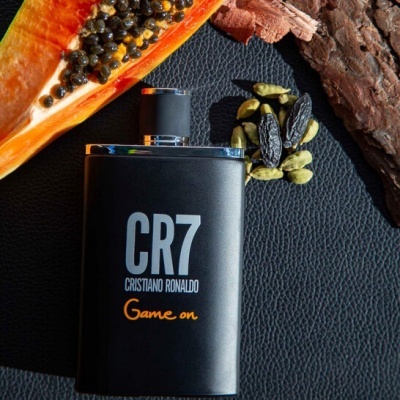 Frasco preto de perfume CR7 Cristiano Ronaldo ao lado de papaia, cardamomo e casca de árvore.