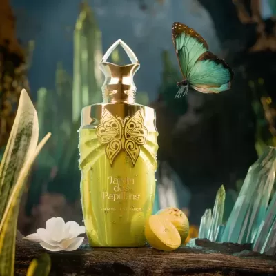 Frasco de perfume verde com tampa dourada e borboleta, limão cortado, flor branca e borboleta azul em ambiente natural