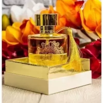Frasco de perfume dourado com penduricalho em caixa sobre superfície com flores ao fundo
