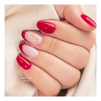 Unhas pintadas com verniz vermelho e decoração dourada numa mão sobre tecido bege
