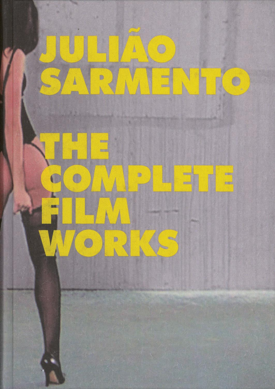 Julião Sarmento – The Complete Film Works Capa de livro cinza com texto amarelo e parte do corpo de pessoa com meia preta e sapatos de salto