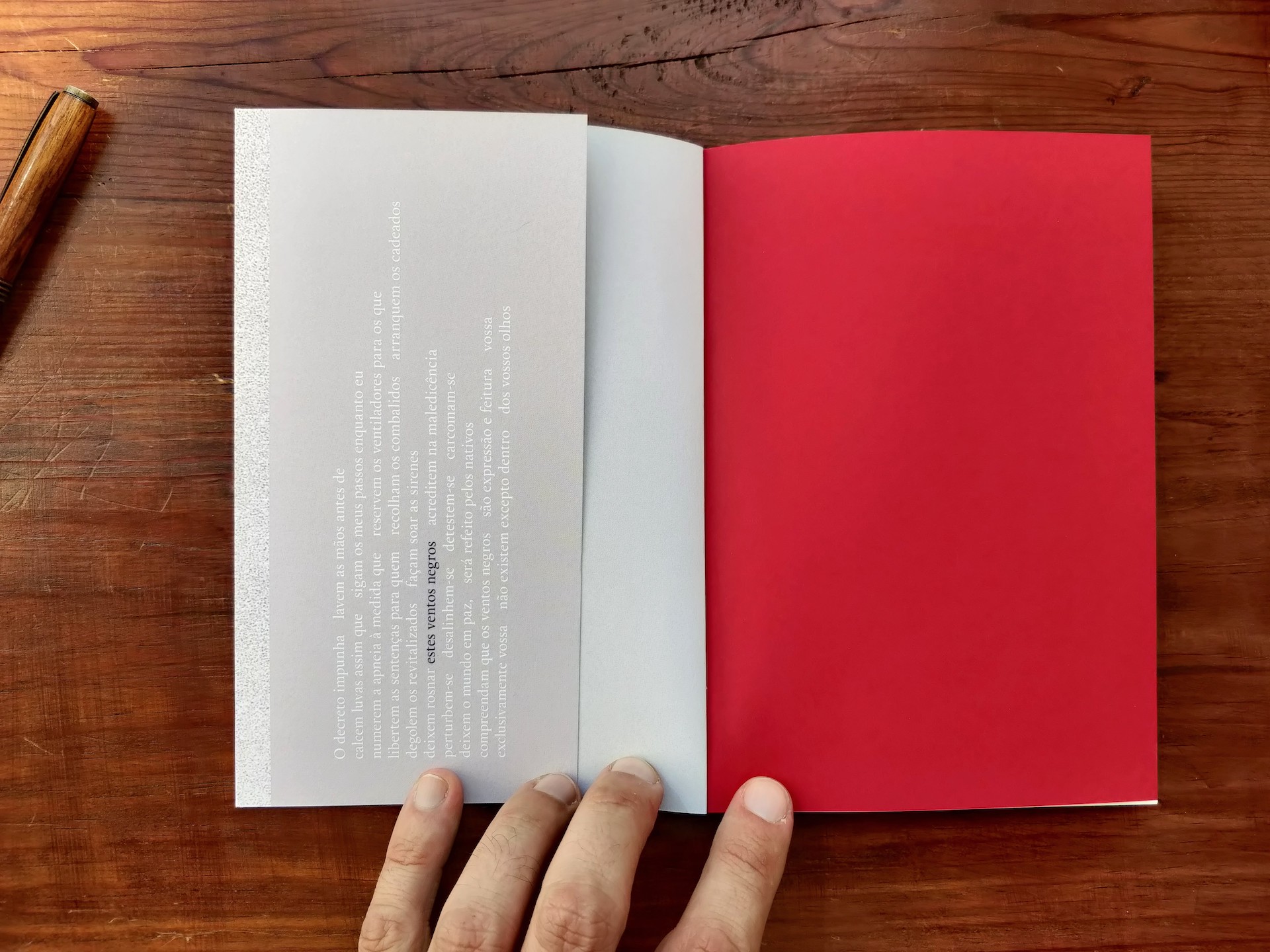 estes ventos negros Livro aberto com capa vermelha e texto em página cinza claro sobre mesa de madeira