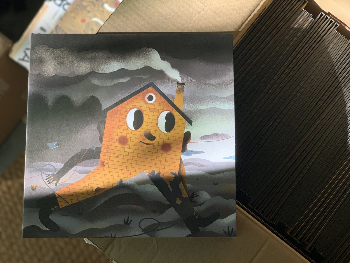 As casas: Romarigães e Outras Histórias Capa de disco com ilustração de casa amarela caricatural a fumar cachimbo, em cima de caixas de discos.