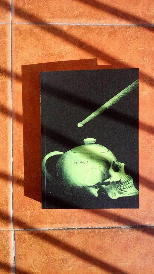 Bestiário #1 Livro com capa preta e ilustração verde de crânio em forma de bule sobre chão de azulejos alaranjados iluminado pelo sol.