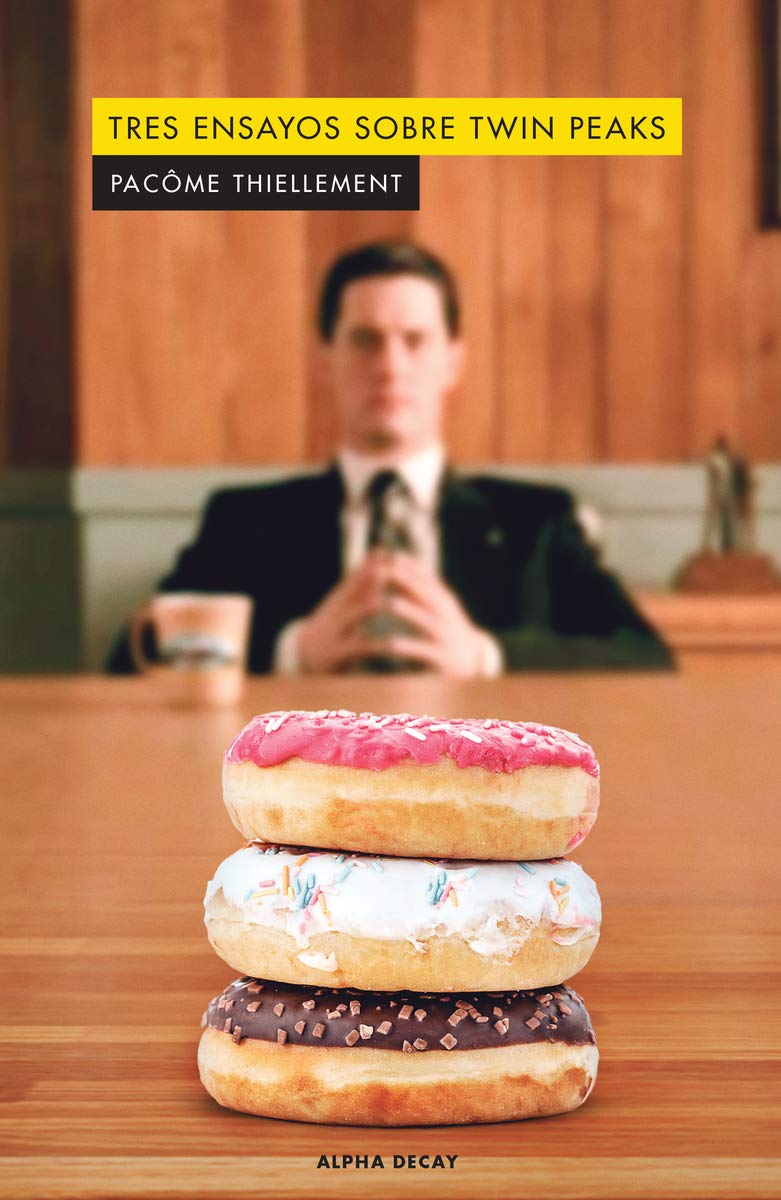 Tres ensayos sobre Twin Peaks Livro com imagem de três donuts empilhados e homem desfocado ao fundo sentado à mesa