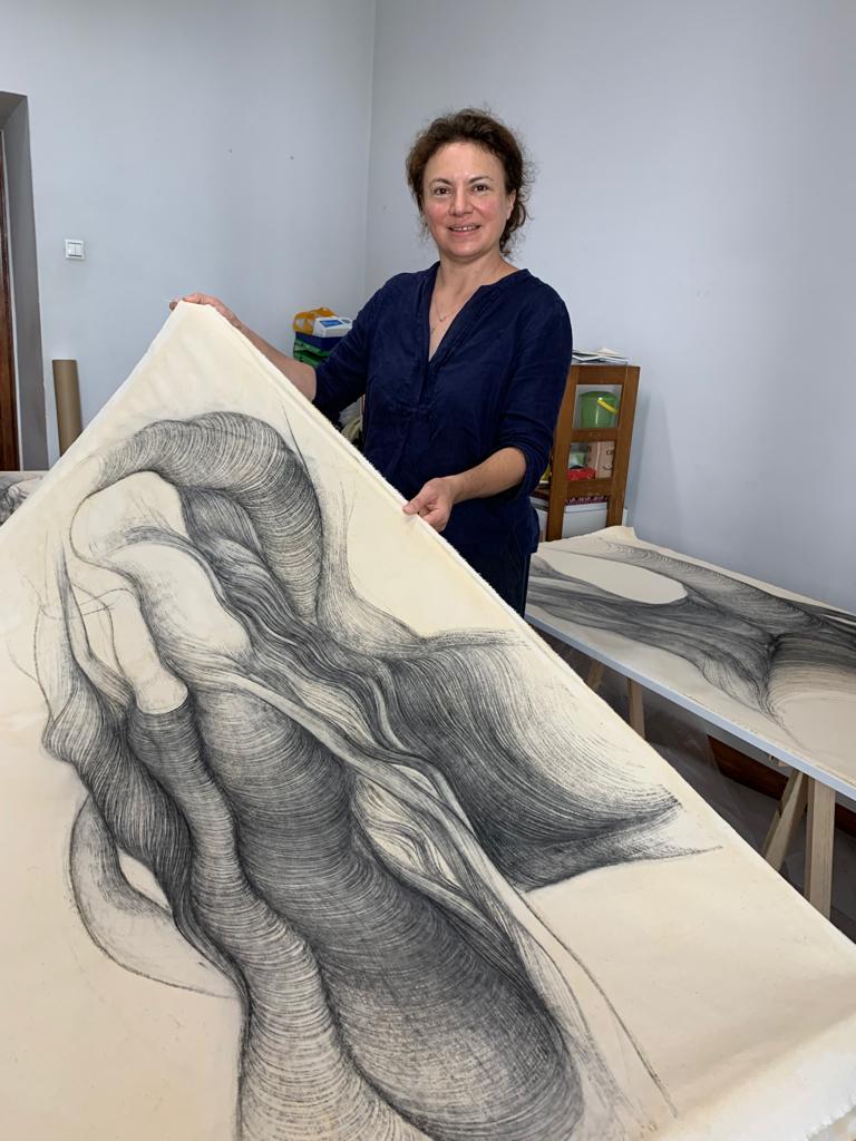 Do Jardim Tropical ao Carvão Vegetal: O Desenho na Linha das Metamorfoses I/II - Du Jardin Tropical au Fusain: Le Dessin au Fil de Ses Métamorphoses I/II Desenho abstrato a carvão em papel creme segurado por mulher numa sala branca