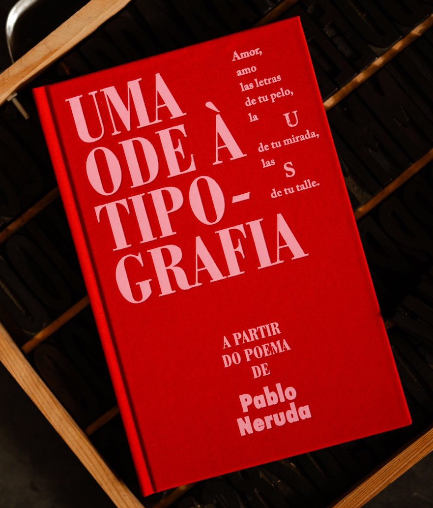 «Uma Ode à Tipografia». A partir do poema de Pablo Neruda Livro vermelho com texto branco sobre tipografia e poema de Pablo Neruda numa superfície preta com moldura de madeira.