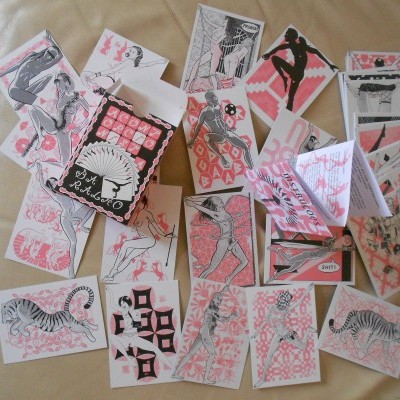 Várias cartas ilustradas a preto, branco e rosa espalhadas com caixa preta 'ARTIST TRADING CARDS'