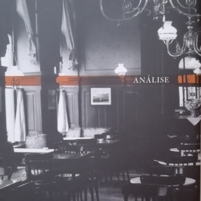 Interior de café clássico em preto e branco com mesas, cadeiras e candeeiros, texto ANÁLISE visível