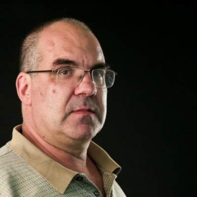 Homem calvo de óculos usando camisa bege em fundo preto